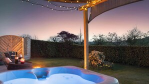A hot tub with a wooden pergola overhead, surrounded by a hedge and a garden with flowers. - Scar View - Getaway for Two | Ridgestone (Kendal)