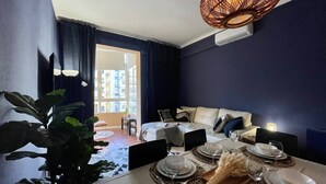Un comedor con una mesa lista para cuatro personas, un sofá al fondo y un ventanal con cortinas.