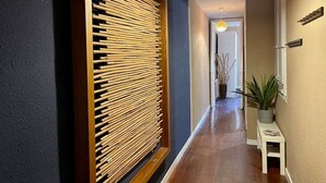 Un pasillo con un biombo de listones de madera, una lámpara colgante, una planta en maceta y una pequeña mesa con una planta.