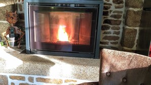 A fireplace with a stone wall backdrop, a leather armchair in front, and a decorative fox figure to the left. - La petite corbière ⭐⭐⭐ Between bocage and sea (Jullouville)