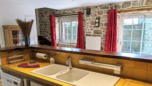 A kitchen with a stone wall, a wooden countertop, a double sink, and red curtains. - La petite corbière ⭐⭐⭐ Between bocage and sea (Jullouville)