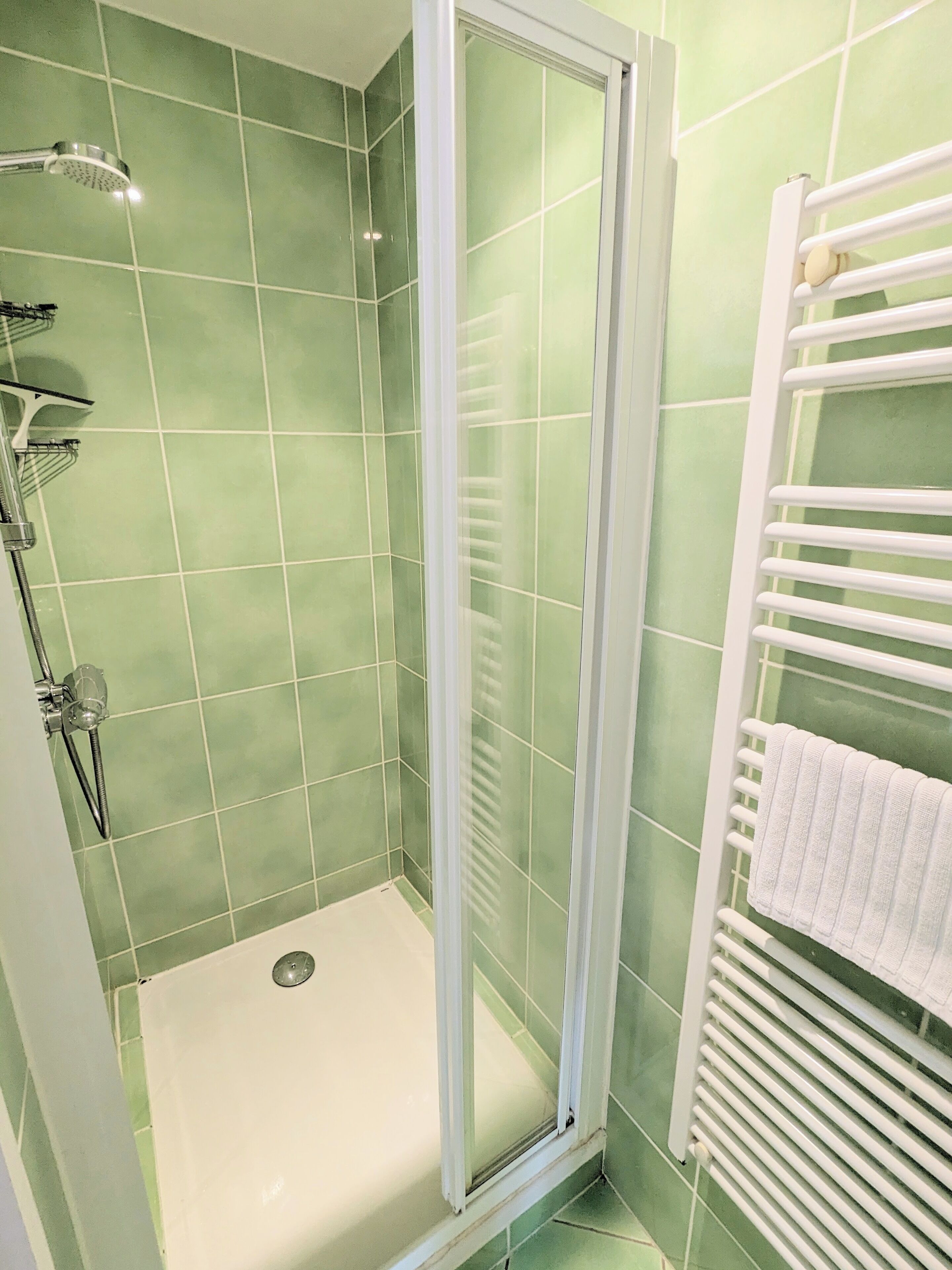 A bathroom with a glass-enclosed shower, a white towel rack, and green-tiled walls.