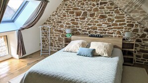 A bedroom with a stone wall, a skylight, a bed with pillows, a nightstand, and a lamp. - La petite corbière ⭐⭐⭐ Between bocage and sea (Jullouville)