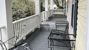 Eine überdachte Veranda mit Holzboden und Metallstühlen.