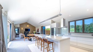 A modern kitchen with a large island, white cabinetry, and a view of greenery outside. - Serenity on Ruby Ridge (Wānaka)