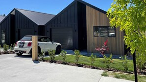 A modern two-story house with a garage, a white car parked in front, and a well-maintained lawn with small shrubs.