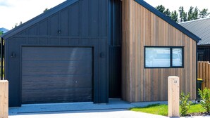 A modern building with a dark facade and a wooden section, featuring a garage door and a window.