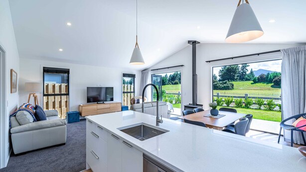 A modern kitchen with a large island, a dining area with a table and chairs, a sofa, and a TV.