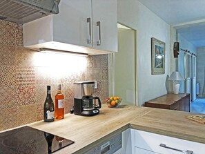 Una cocina con baldosas estampadas, una cafetera, una botella y un cuenco de fruta.