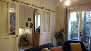 A cozy living room with a dark blue sofa, a wooden desk, and a large window with a view of trees. - Beautiful furnished and comfortable apartment in the center of Bordeaux (Bordeaux)