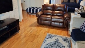 A living room with a brown leather sofa, a television on a stand, a patterned rug, and a bed in the background. - Classic Charm Close To Lake (Canyon Lake)