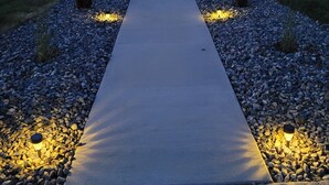 A pathway with embedded lighting, flanked by small shrubs and pebbles, leading to a building entrance. - Cleveland Place (Meeker)