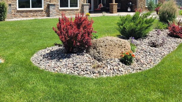 A two-story house with a stone facade, a balcony with outdoor seating, and a well-maintained lawn with shrubs and flowers. - Cleveland Place (Meeker)