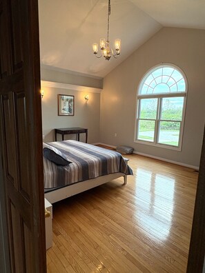A bedroom with a bed, a chandelier, a window, and a painting on the wall.