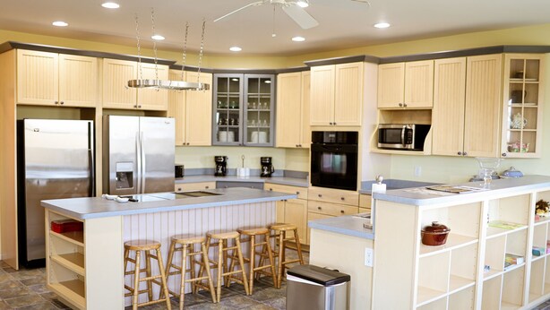 A kitchen with light wooden cabinets, stainless steel appliances, a central island with stools, and a ceiling fan. - Holland Estate (Williamstown)