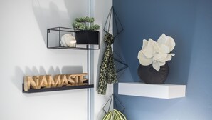 A wall with a shelf displaying a wooden sign, a black shelf with a plant, and a white vase with flowers. - City Nest Apartment by Cloudkeys (Athens)