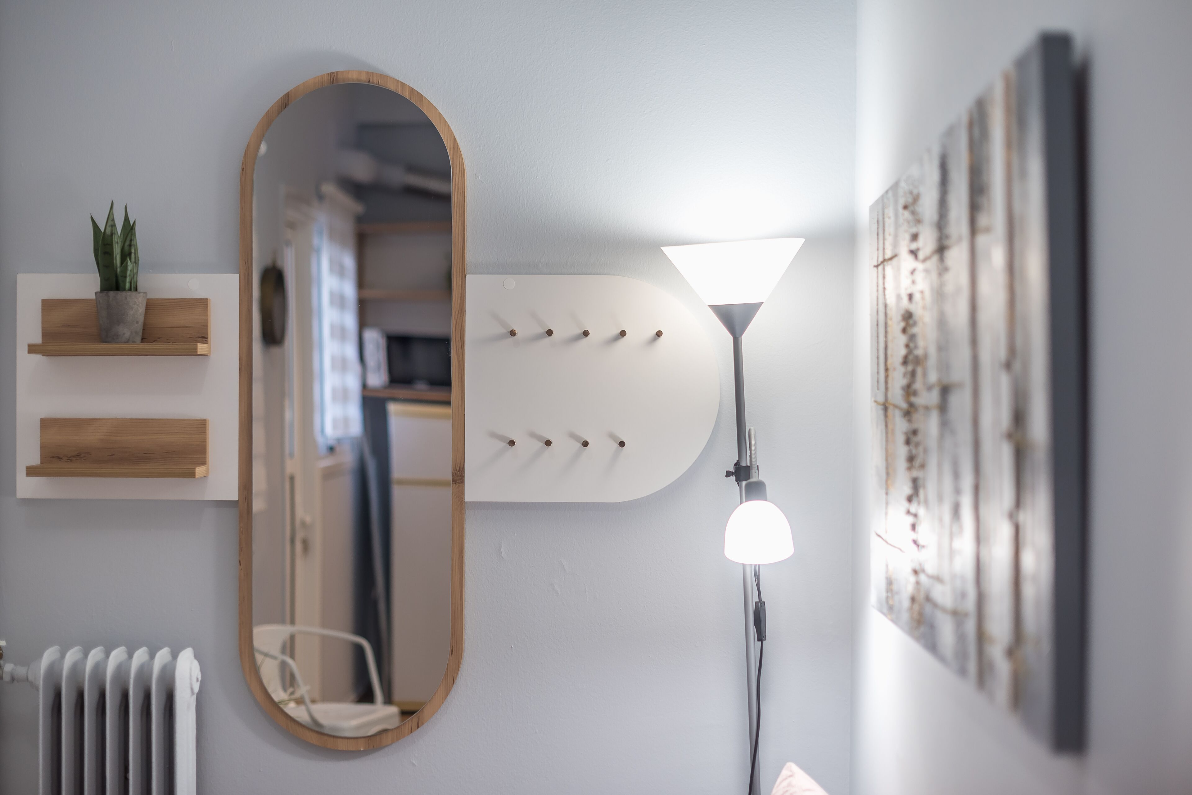 A bathroom with a wooden-framed mirror, a wall-mounted light fixture, a radiator, and a shelf with a potted plant.