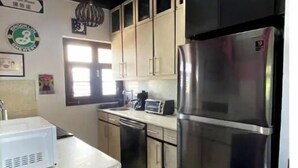 Una cocina con un refrigerador de acero inoxidable, un microondas y un lavavajillas. Hay armarios de madera y un piso de baldosas a cuadros.