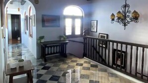 Un pasillo con piso a cuadros, una escalera con barandilla negra y un candelabro.