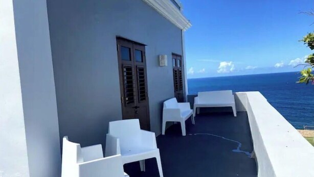 Un balcón con sillas y una mesa de plástico blanco, con vista al océano.