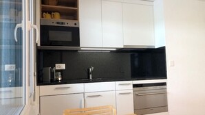 A kitchen with white cabinets, a black countertop, a wooden table, and a window.
