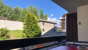 A balcony with a red table and chairs, overlooking a building and a tree.