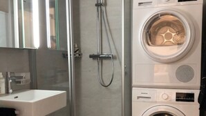 A modern bathroom with a glass-enclosed shower, a sink, a toilet, and a stacked washer and dryer.