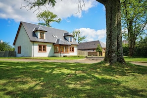 A two-story house with a sloped roof, a front porch, and a large tree in the foreground.