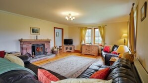 A living room with a fireplace, a television, and a sofa with cushions. - Country farmhouse sleeps 9 with enclosed garden and games barn. (Blairgowrie, Perthshire)