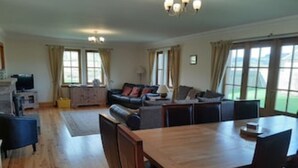 A spacious living area with a wooden dining table, multiple sofas, and a television. - Country farmhouse sleeps 9 with enclosed garden and games barn. (Blairgowrie, Perthshire)