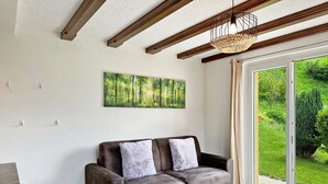 A modern living room with a sofa, a coffee table, and a large window with a view of greenery. - Chez Tonton à 5mns de Sion (Sion)