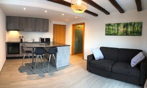 A modern kitchen with grey cabinets, a central island with stools, a dark sofa, and a forest-themed painting on the wall.