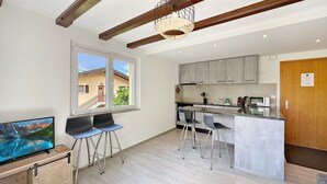 A modern kitchen with a large window, bar stools, and a TV on a wooden stand. - Chez Tonton à 5mns de Sion (Sion)