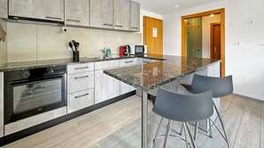 A modern kitchen with a granite countertop, stainless steel appliances, and bar stools. - Chez Tonton à 5mns de Sion (Sion)