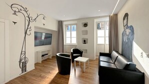 Un salon moderne avec un téléviseur à écran plat, un canapé en cuir noir, une table basse blanche et un fauteuil noir.