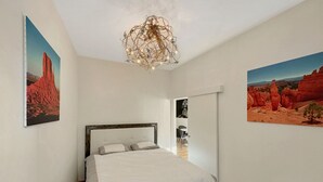 Une chambre à coucher avec un lit, des murs blancs et deux tableaux représentant des paysages.
