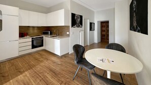 Une cuisine moderne avec des meubles blancs, un four à micro-ondes et un évier. On y trouve également un coin repas avec une table ronde et deux chaises.