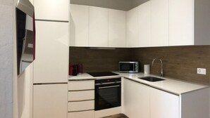 Une cuisine de taille réduite avec des meubles blancs, un four à micro-ondes, une cuisinière et un évier.