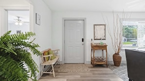 A modern interior with a wooden bench, a door, a small table with a vase, and a large plant. - Spacious Renovated Home with Fenced Yard (Springdale)