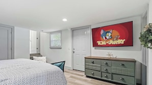 A bedroom with a bed, a dresser, a television displaying 'Tom and Jerry', and a window with blinds. - Spacious Renovated Home with Fenced Yard (Springdale)
