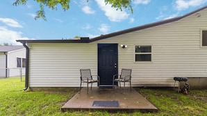 A single-story house with a front porch, two chairs, a door, and a small grill. - Spacious Renovated Home with Fenced Yard (Springdale)