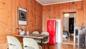 A wooden-paneled room with a dining table and chairs, a red refrigerator, and a kitchen area visible through an open door. - The One and Only in Sion (Sion)