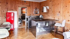 A compact kitchen with wooden paneling, a red refrigerator, stainless steel appliances, and a dining area with a table and chairs. - The One and Only in Sion (Sion)