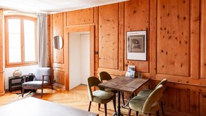 A wooden-paneled room with a dining table and four chairs, a small table with a lamp, and a door leading to another room. - The One and Only in Sion (Sion)