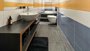 A modern bathroom with a large mirror, a sink, a toilet, and a bathtub. - The One and Only in Sion (Sion)