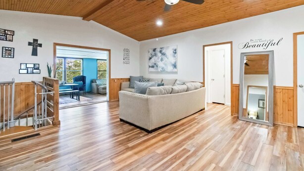 A spacious living room with a wooden ceiling, a ceiling fan, a sofa, a staircase, and a large window. - War Eagle Getaway (Springdale)