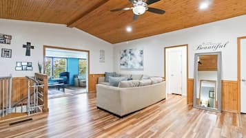 A spacious living room with a wooden ceiling, a ceiling fan, a sofa, a staircase, and a large window.