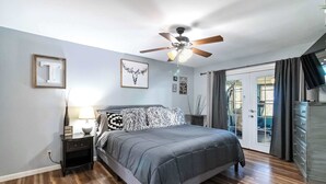 A bedroom with a bed, a nightstand, a ceiling fan, and a view of the outdoors. - War Eagle Getaway (Springdale)