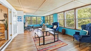 A spacious room with a wooden floor, a blue sofa, a table with benches, and large windows. - War Eagle Getaway (Springdale)