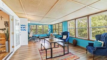 A spacious room with a wooden floor, a blue sofa, a table with benches, and large windows.